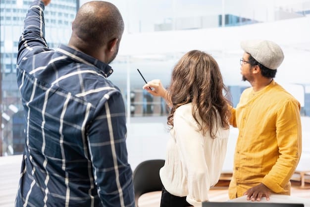 A close-up of a diverse group of people examining blueprints in a brightly lit office. One person is pointing to a structure on the plan.