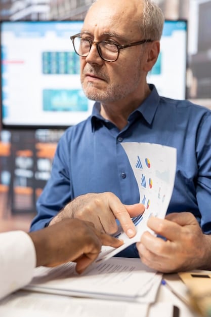 A close-up shot of a financial analyst reviewing detailed financial statements and reports on a computer screen. The analyst is wearing glasses and has a focused expression, highlighting the meticulous nature of financial analysis. The background is blurred, with elements of an office environment visible.